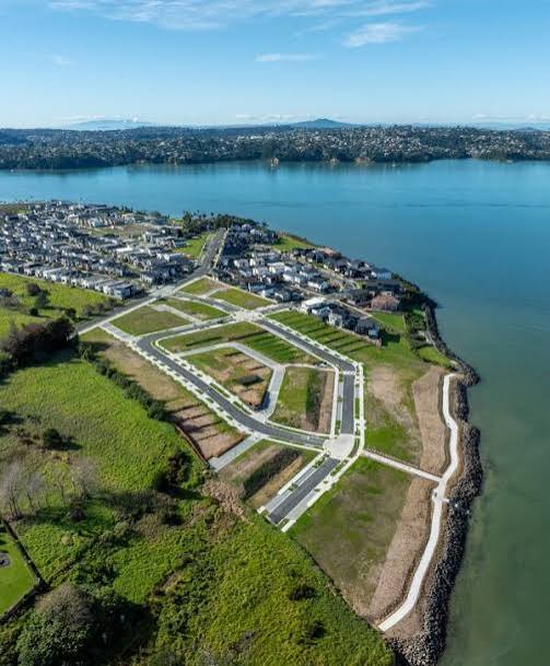 Aerial view of a coastal Auckland subdivision with completed roading beside the harbour