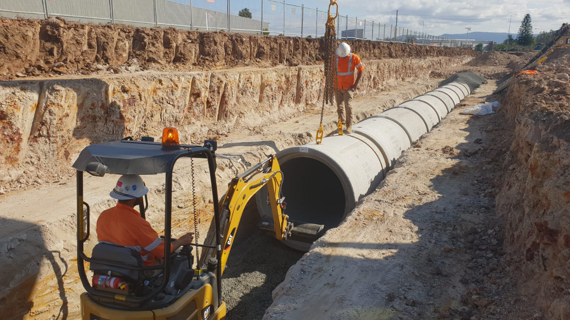 Large diameter concrete pipeline being installed in a deep trench by an excavator